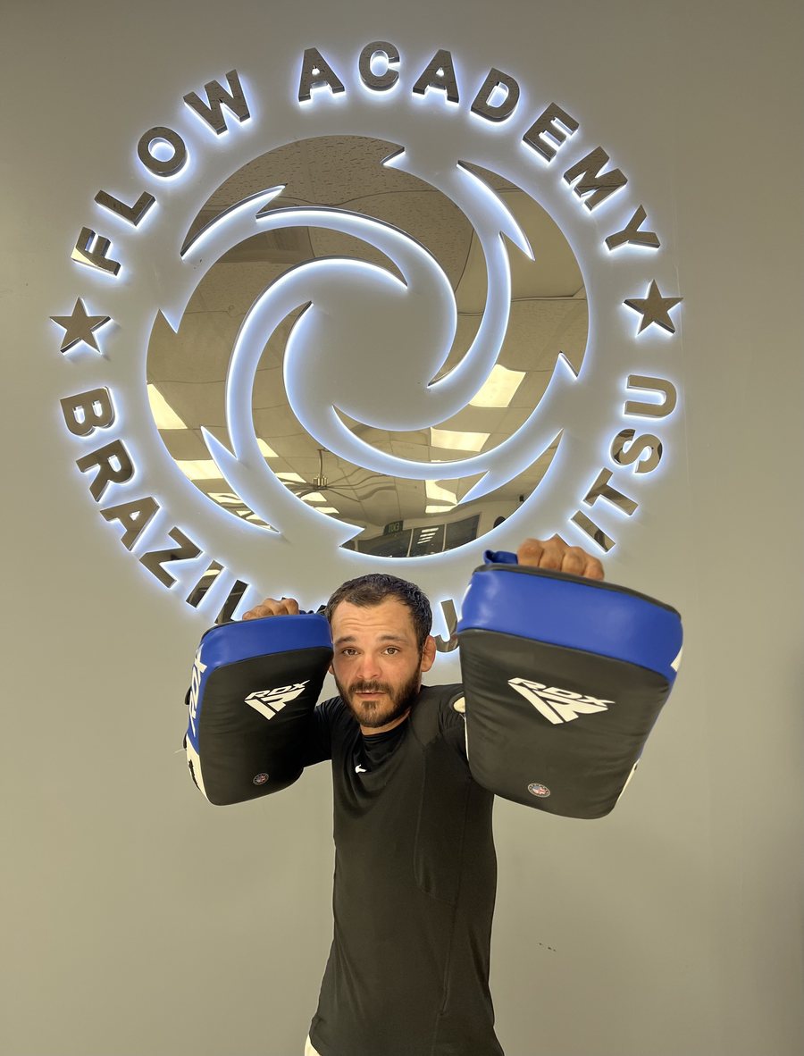 El Coach Adrian sosteniendo paos de Muay Thai bajo el letrero de Flow Academy